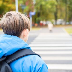 Student wearing a backpack approaching a marked crosswalk on the way to school