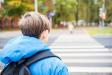 Student wearing a backpack approaching a marked crosswalk on the way to school